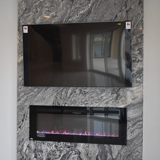 インディアナポリスの巨大なコンテンポラリースタイルのおしゃれな地下室 (半地下 (ドアあり)、グレーの壁、吊り下げ式暖炉、石材の暖炉まわり) の写真