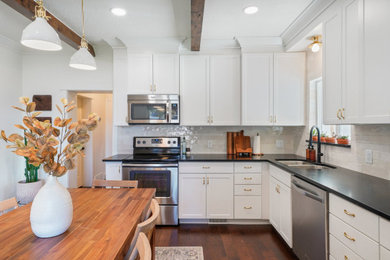 Inspiration for a small farmhouse l-shaped dark wood floor, brown floor and exposed beam enclosed kitchen remodel in Salt Lake City with a double-bowl sink, shaker cabinets, white cabinets, granite countertops, white backsplash, ceramic backsplash, stainless steel appliances and black countertops