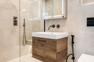 Small modern ensuite bathroom in London with flat-panel cabinets, dark wood cabinets, a walk-in shower, a wall mounted toilet, beige tiles, ceramic tiles, ceramic flooring, a built-in sink, beige floors, a single sink and a floating vanity unit.