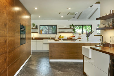 Mid-sized mid-century modern l-shaped porcelain tile, gray floor and vaulted ceiling eat-in kitchen photo in San Francisco with a farmhouse sink, flat-panel cabinets, medium tone wood cabinets, brown backsplash, wood backsplash, paneled appliances, an island, white countertops and wood countertops
