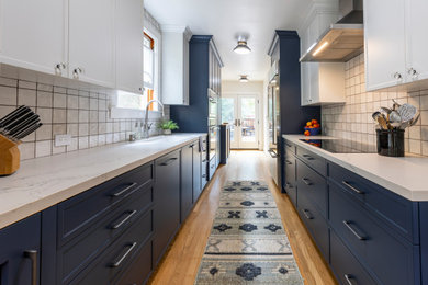 サクラメントにある高級な中くらいなトランジショナルスタイルのおしゃれなキッチン (一体型シンク、シェーカースタイル扉のキャビネット、青いキャビネット、クオーツストーンカウンター、白いキッチンパネル、磁器タイルのキッチンパネル、シルバーの調理設備、無垢フローリング、アイランドなし、茶色い床、白いキッチンカウンター) の写真