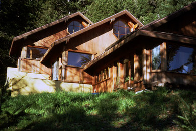 Diseño de fachada de casa marrón de estilo americano grande a niveles con revestimiento de madera, tejado a cuatro aguas y tejado de teja de madera
