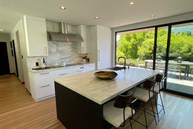 Minimalist medium tone wood floor open concept kitchen photo in San Francisco with an undermount sink, flat-panel cabinets, black cabinets, marble countertops, white backsplash, marble backsplash, white appliances, an island and white countertops