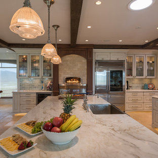 This is an example of a large mediterranean kitchen pantry in Hawaii with a farmhouse sink, raised-panel cabinets, white cabinets, green splashback, ceramic splashback, stainless steel appliances, multiple islands and beige floor.