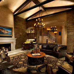 Modelo de salón abierto, mediterráneo, con paredes beige, chimenea tradicional, marco de chimenea de piedra y televisor retractable