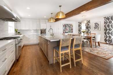 Large transitional l-shaped eat-in kitchen in Denver with an undermount sink, raised-panel cabinets, white cabinets, multi-coloured splashback, subway tile splashback, stainless steel appliances, dark hardwood floors, with island, brown floor, white benchtop and exposed beam.