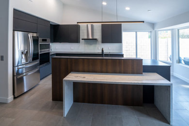 Eat-in kitchen - small industrial l-shaped ceramic tile and gray floor eat-in kitchen idea in Phoenix with a drop-in sink, flat-panel cabinets, black cabinets, granite countertops, white backsplash, glass tile backsplash, stainless steel appliances, an island and black countertops
