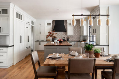 Eat-in kitchen - large craftsman l-shaped light wood floor eat-in kitchen idea in Other with a farmhouse sink, shaker cabinets, white cabinets, wood countertops, multicolored backsplash, white appliances, an island and brown countertops