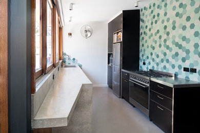 Modern eat-in kitchen in Adelaide with recessed-panel cabinets, black cabinets, green splashback, ceramic splashback, black appliances, concrete floors and beige floor.