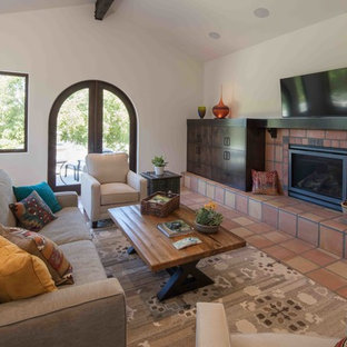 Imagen de salón abierto, mediterráneo, grande, con paredes blancas, chimenea tradicional, marco de chimenea de baldosas y/o azulejos, televisor colgado en la pared, suelo naranja y suelo de baldosas de terracota