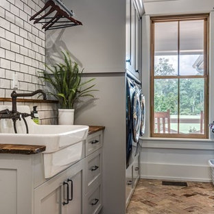 Photo of a medium sized rural galley separated utility room in Nashville with a belfast sink, shaker cabinets, grey cabinets, wood worktops, grey walls, brick flooring, a side by side washer and dryer, brown floors and brown worktops.
