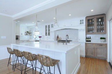 Inspiration for a large transitional u-shaped eat-in kitchen in Los Angeles with a farmhouse sink, recessed-panel cabinets, white cabinets, quartzite benchtops, white splashback, stone slab splashback, stainless steel appliances, light hardwood floors, with island, beige floor and white benchtop.