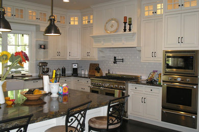 Mid-sized elegant l-shaped dark wood floor and brown floor open concept kitchen photo in Sacramento with a farmhouse sink, raised-panel cabinets, white cabinets, granite countertops, white backsplash, subway tile backsplash, paneled appliances and an island