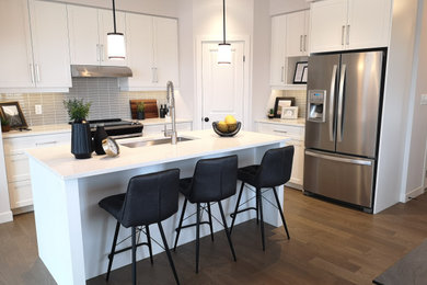 Inspiration for a modern l-shaped medium tone wood floor and brown floor open concept kitchen remodel in Other with an undermount sink, shaker cabinets, white cabinets, quartz countertops, subway tile backsplash, stainless steel appliances, an island and white countertops