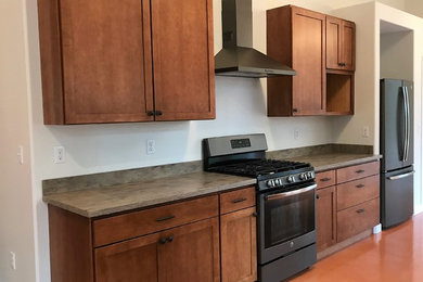Example of a trendy galley concrete floor kitchen design in Other with a drop-in sink, shaker cabinets, medium tone wood cabinets, solid surface countertops, stainless steel appliances and no island