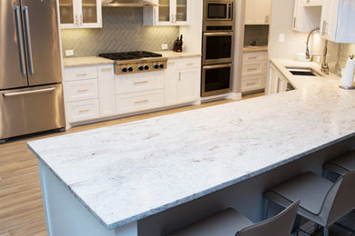 Example of a large transitional u-shaped porcelain tile and brown floor eat-in kitchen design in Dallas with an undermount sink, shaker cabinets, white cabinets, granite countertops, gray backsplash, glass tile backsplash, stainless steel appliances and a peninsula
