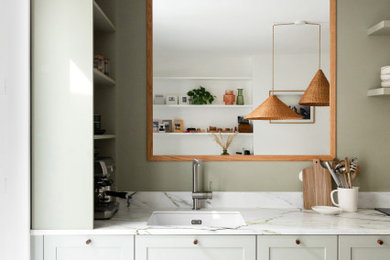 Cette photo montre une cuisine américaine linéaire scandinave avec un placard à porte shaker, des portes de placards vertess, plan de travail en marbre, une crédence blanche, une crédence en marbre, un sol blanc et un plan de travail blanc.