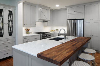 Example of a mid-sized transitional l-shaped medium tone wood floor, brown floor and exposed beam enclosed kitchen design in Miami with a single-bowl sink, shaker cabinets, beige cabinets, quartz countertops, white backsplash, porcelain backsplash, stainless steel appliances, an island and white countertops