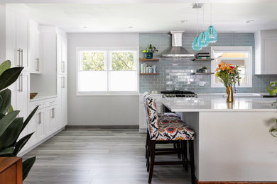 デンバーにあるお手頃価格の中くらいなトランジショナルスタイルのおしゃれなキッチン (エプロンフロントシンク、シェーカースタイル扉のキャビネット、白いキャビネット、クオーツストーンカウンター、緑のキッチンパネル、ガラスタイルのキッチンパネル、シルバーの調理設備、ラミネートの床、グレーの床、白いキッチンカウンター) の写真