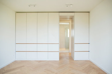 Modernes Ankleidezimmer mit flächenbündigen Schrankfronten, weißen Schränken und hellem Holzboden in Berlin