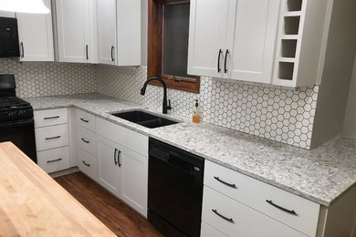 Example of a mid-sized minimalist l-shaped vinyl floor and brown floor eat-in kitchen design in Other with an undermount sink, shaker cabinets, white cabinets, quartz countertops, white backsplash, porcelain backsplash, black appliances and an island