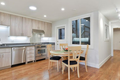 Mid-sized minimalist l-shaped medium tone wood floor eat-in kitchen photo in Boston with an undermount sink, flat-panel cabinets, light wood cabinets, solid surface countertops, stainless steel appliances and no island
