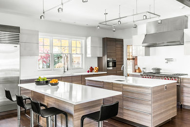Design ideas for a mid-sized contemporary l-shaped eat-in kitchen in Boston with white splashback, stainless steel appliances, medium hardwood floors, multiple islands, an undermount sink, flat-panel cabinets, light wood cabinets, solid surface benchtops and ceramic splashback.