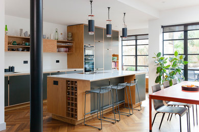 Large modern eat-in kitchen in London with flat-panel cabinets, grey cabinets, quartzite benchtops, white splashback, medium hardwood floors, with island and white benchtop.