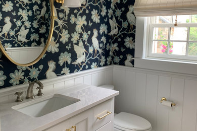 Example of a beach style vinyl floor and wainscoting powder room design in Boston with shaker cabinets, white cabinets, a two-piece toilet, an undermount sink, quartzite countertops, white countertops and a built-in vanity