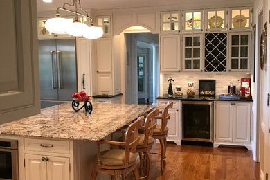 Inspiration for a large traditional u-shaped open plan kitchen in New York with an undermount sink, raised-panel cabinets, white cabinets, granite benchtops, grey splashback, stone tile splashback, stainless steel appliances, medium hardwood floors and with island.