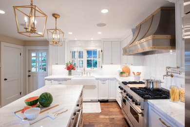 Photo of a traditional l-shaped kitchen in Seattle with a farmhouse sink, shaker cabinets, white cabinets, white splashback, stone slab splashback, stainless steel appliances and white benchtop.