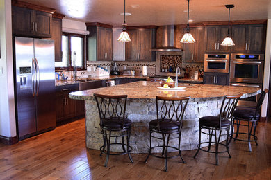 Example of a large trendy l-shaped medium tone wood floor and brown floor open concept kitchen design in Denver with a farmhouse sink, granite countertops, stone tile backsplash, stainless steel appliances, shaker cabinets, dark wood cabinets, gray backsplash and an island