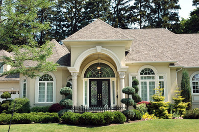 Example of a large classic beige one-story concrete house exterior design in New York with a hip roof and a shingle roof