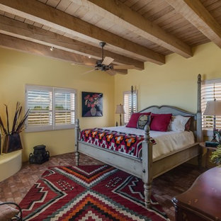 Bild på ett mellanstort amerikanskt huvudsovrum, med gula väggar, tegelgolv, en öppen hörnspis, en spiselkrans i gips och brunt golv