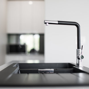 Large modern galley kitchen pantry in Sydney with a drop-in sink, flat-panel cabinets, white cabinets, quartz benchtops, black splashback, glass sheet splashback, stainless steel appliances, plywood floors, with island and grey floor.