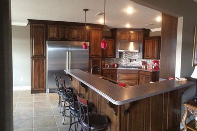 Inspiration for a mid-sized transitional u-shaped limestone floor eat-in kitchen remodel in Other with an undermount sink, raised-panel cabinets, medium tone wood cabinets, solid surface countertops, gray backsplash, glass tile backsplash, stainless steel appliances and an island