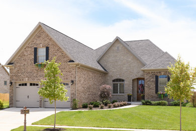 Mid-sized transitional beige two-story brick house exterior idea in Other with a hip roof and a shingle roof