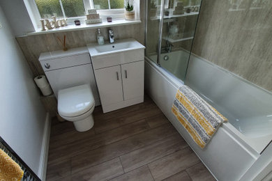 Design ideas for a medium sized contemporary grey and brown family bathroom in Surrey with flat-panel cabinets, white cabinets, a built-in bath, a shower/bath combination, a one-piece toilet, beige walls, vinyl flooring, a built-in sink, grey floors, a single sink, a floating vanity unit and panelled walls.