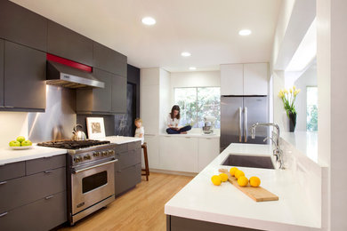 This is an example of a mid-sized transitional galley eat-in kitchen in Los Angeles with an undermount sink, flat-panel cabinets, grey cabinets, solid surface benchtops, stainless steel appliances, light hardwood floors, with island and brown floor.