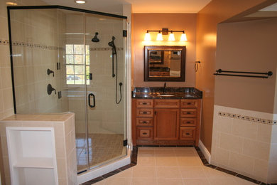 Large traditional master bathroom in Baltimore with raised-panel cabinets, medium wood cabinets, a drop-in tub, a corner shower, beige tile, porcelain tile, brown walls, porcelain floors, an undermount sink, onyx benchtops, beige floor and a hinged shower door.