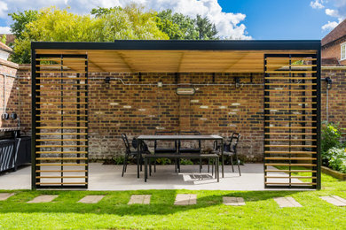 This is an example of a medium sized modern back full sun pergola in Hertfordshire with natural stone paving.