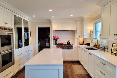 Foto på ett stort vintage vit kök, med en undermonterad diskho, skåp i shakerstil, vita skåp, marmorbänkskiva, vitt stänkskydd, stänkskydd i marmor, integrerade vitvaror, mörkt trägolv, en köksö och brunt golv
