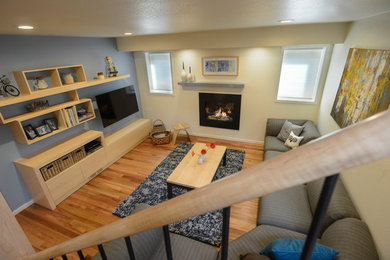 Photo of a small modern basement in Denver with yellow walls, medium hardwood floors and a standard fireplace.