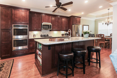 Example of a mid-sized classic galley medium tone wood floor and brown floor open concept kitchen design in Atlanta with an undermount sink, beaded inset cabinets, dark wood cabinets, granite countertops, beige backsplash, porcelain backsplash, stainless steel appliances, an island and multicolored countertops