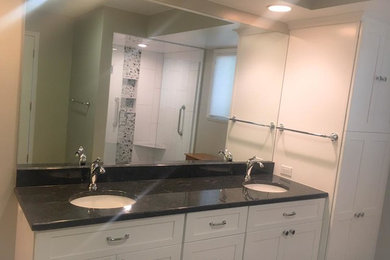 Inspiration for a large contemporary master bathroom in Detroit with shaker cabinets, white cabinets, a double shower, a one-piece toilet, beige walls, porcelain floors, an undermount sink, granite benchtops, a hinged shower door and black benchtops.