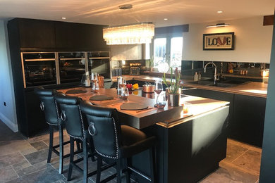 This is an example of a large modern u-shaped open plan kitchen in Other with a double-bowl sink, flat-panel cabinets, black cabinets, laminate countertops, metallic splashback, mirror splashback, black appliances, slate flooring, an island, multi-coloured floors and beige worktops.