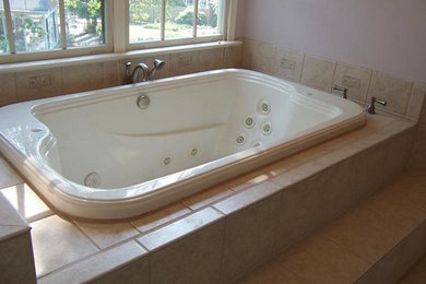 Example of a mid-sized classic master beige tile and ceramic tile travertine floor alcove shower design in Other with a hot tub, raised-panel cabinets, medium tone wood cabinets, an undermount sink and solid surface countertops