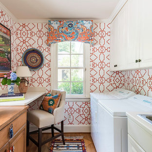 Design ideas for a small traditional galley utility room in Charlotte with composite countertops, a side by side washer and dryer, raised-panel cabinets, a built-in sink, white cabinets, red walls, medium hardwood flooring and brown floors.