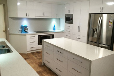 Inspiration for a contemporary u-shaped separate kitchen in Perth with a double-bowl sink, flat-panel cabinets, white cabinets, granite benchtops, grey splashback, glass sheet splashback, stainless steel appliances, medium hardwood floors and with island.