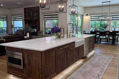 Example of a large trendy l-shaped medium tone wood floor and brown floor open concept kitchen design in Seattle with a farmhouse sink, shaker cabinets, dark wood cabinets, marble countertops, stainless steel appliances, an island and white countertops